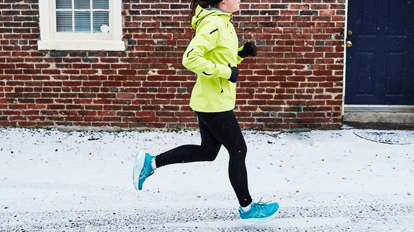 person jogging on a snowy path beside a brick wall and a door