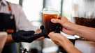 Close-up of a barista handing a cup of takeaway iced coffee to a customer.