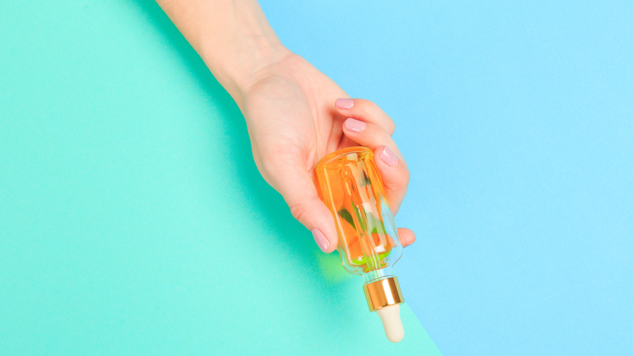 hand holding serum bottle on blue and green background