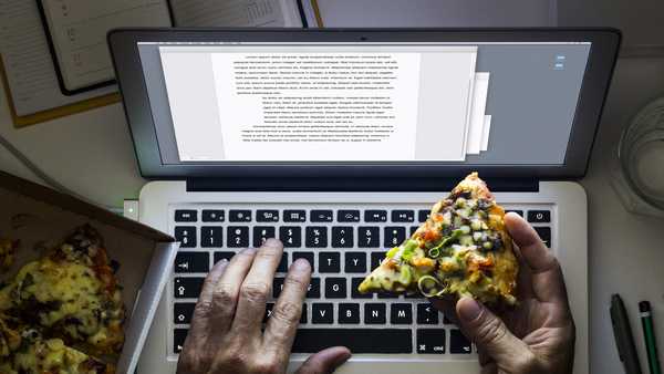 hand holding a pizza while working on a laptop