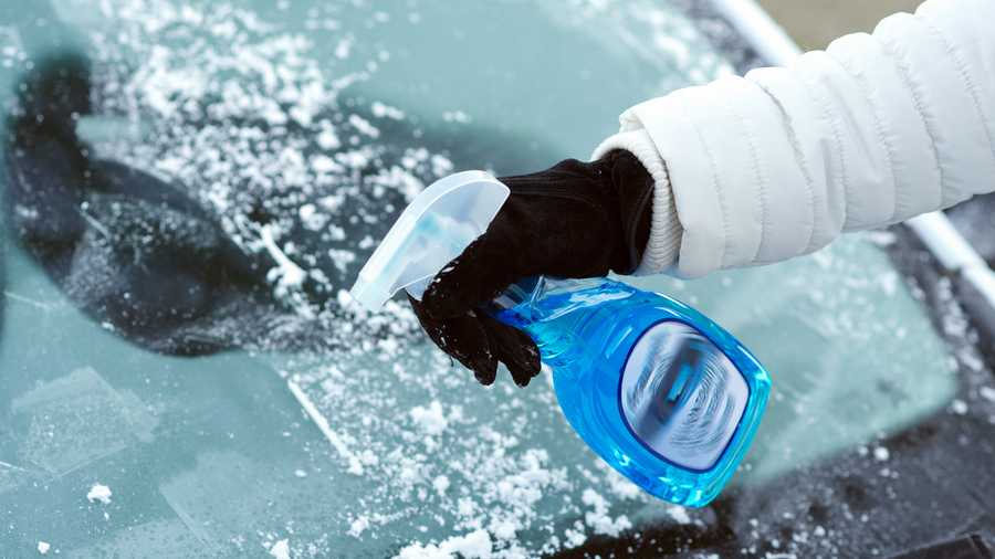 ice scraping and using a defrost spray on car windscreen