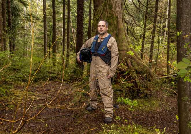 a man wearing firefighting gear poses for a portrait in the woods