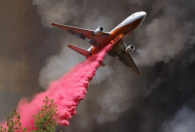 a large plane flying in front of a dark sky dropping pink fire retardant