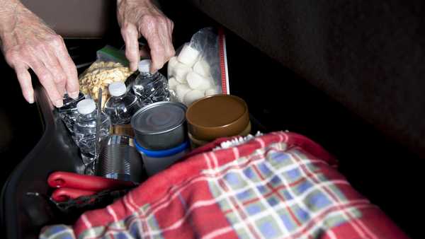 person preparing roadside emergency kit with a red blanket, plastic water bottles, and canned food