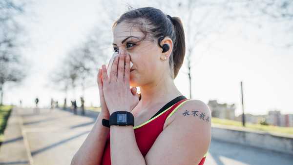 sporty young woman with wireless earphones blowing her nose