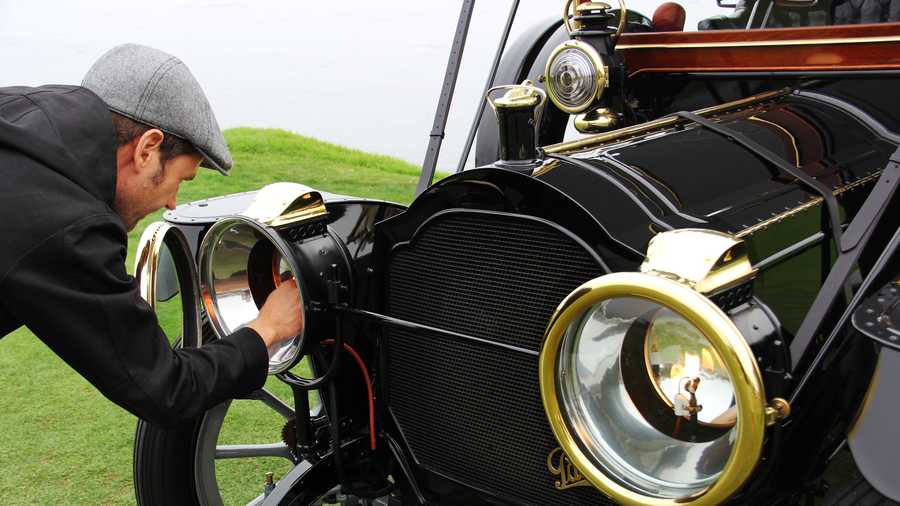 Derek Hill, a concours judge and owner of this 1912 Packard, ignites a flame inside the Packard's headlights.