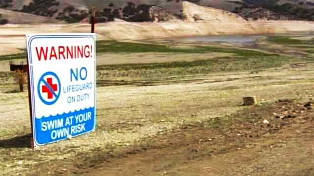 A sign reading "swim at your own risk" is seen at Lake San Antonio where water dried out.
