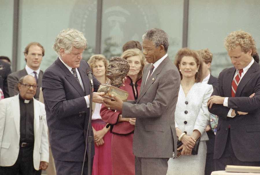 Nelson Mandela receives a bust of the late president John F. Kennedy from the president's brother Sen. Edward Kennedy, left, during a ceremony at the John F. Kennedy library, June 23, 1990. At far right is Jacqueline Kennedy Onassis. Eunice Shriver, in red dress, sister of Sen. Kennedy looks on behind Mandela. At right is Joe Kennedy II, son of Robert Kennedy.