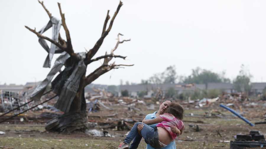 A woman carries her child through a field near the collapsed Plaza Towers Elementary School in Moore, Okla.