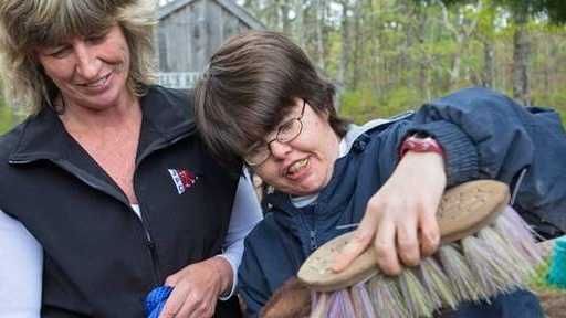 Instructor Kris Thompson holds Jake's leash as Diana Gaudet brushes the miniature donkey's fur. The therapy program teaches patience and responsibility.