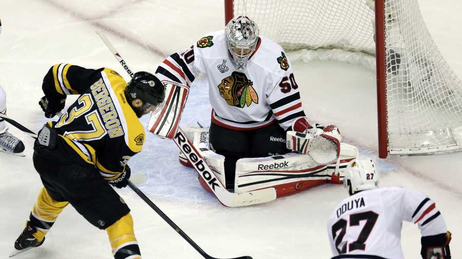 Boston Bruins center Patrice Bergeron (37) moves the puck between Chicago Blackhawks goalie Corey Crawford (50) and defenseman Johnny Oduya (27), of Sweden, during the first period in Game 3 of the NHL hockey Stanley Cup Finals in Boston, Monday, June 17, 2013.