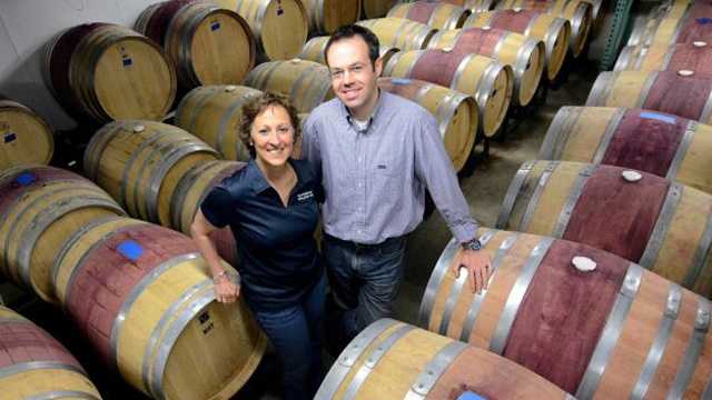 In this June 7, 2013 photo, Donna and Christian Hanson pose with wine casks at Balderdash Cellars in Pittsfield, Mass. The couple started in the basement of their house, then moved to the garage, then moved to the basement of a former bakery on East street. 