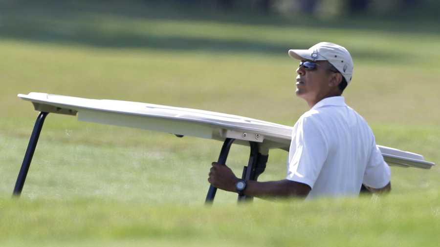 President Barack Obama holds onto a golf cart as he looks toward the green while golfing at Farm Neck Golf Club in Oak Bluffs, Mass., on the island of Martha's Vineyard, Saturday, Aug. 17, 2013.