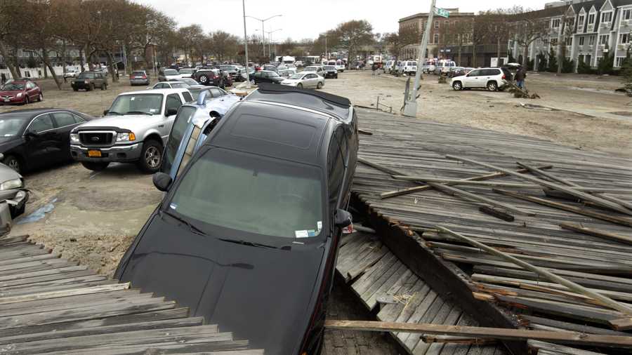 Pedestrians walk past the boardwalk and cars displaced by superstorm Sandy, near Rockaway Beach in the New York City borough of Queens, Tuesday, Oct. 30, 2012, in New York. 