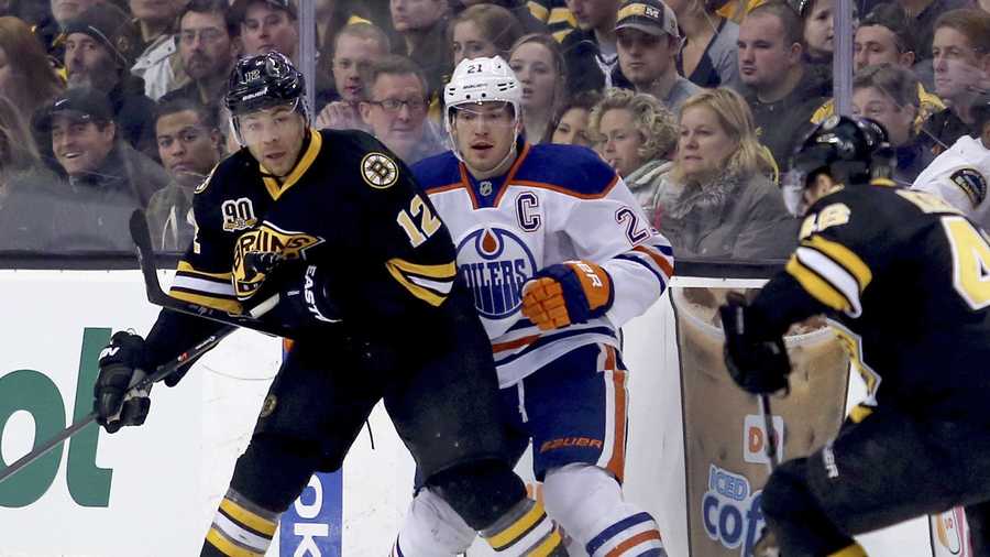 Edmonton Oilers defenseman Andrew Ference (21) is pushed against the boards as Boston Bruins right wing Jarome Iginla (12) passes the puck during the first period of an NHL hockey game, Saturday, Feb. 1, 2014 in Boston. (AP Photo/Mary Schwalm)