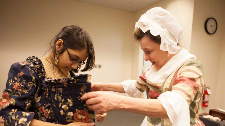 Astha Agarwal, (left), a senior from Newton South High school tried on clothes from the 18th Century with the help of "First Lady Abigail Adams," portrayed by Patricia Bridgman. 