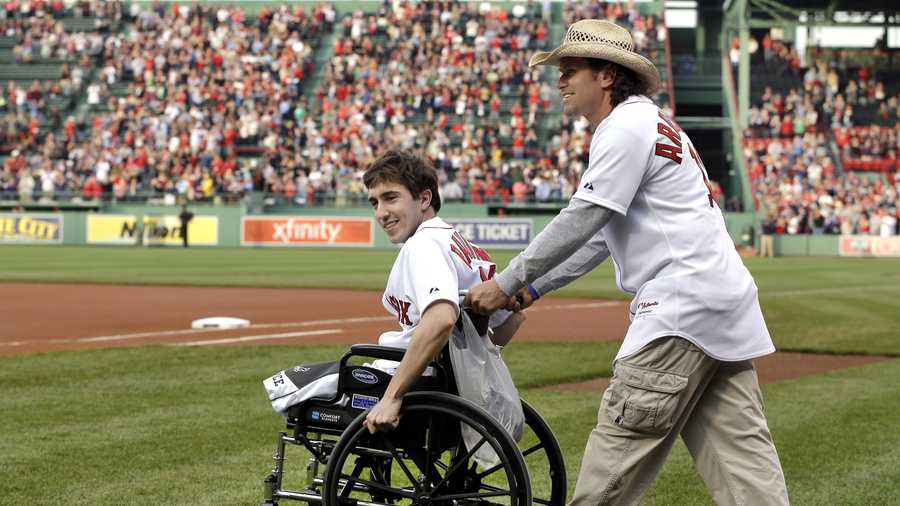 Boston Marathon bombing survivor Jeff Bauman, left, is wheeled out by Carlos Arredondo, the man who helped save his life, to throw out the ceremonial first pitch at Fenway Park prior to a baseball between the Boston Red Sox and the Philadelphia Phillies, May 28, 2013, in Boston.