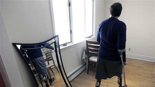 In this March 14, 2014 photo, Jeff Bauman walks past a mirror at his home in Carlisle, Mass. Bauman, who lost both his legs above the knee in the Boston Marathon bombing, played a key role in identifying the men suspected of placing the two devices.