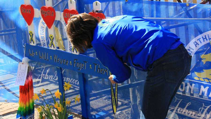 A woman wearing a 2013 Boston Marathon jacket drops off a medal at the memorial at the finish line.
