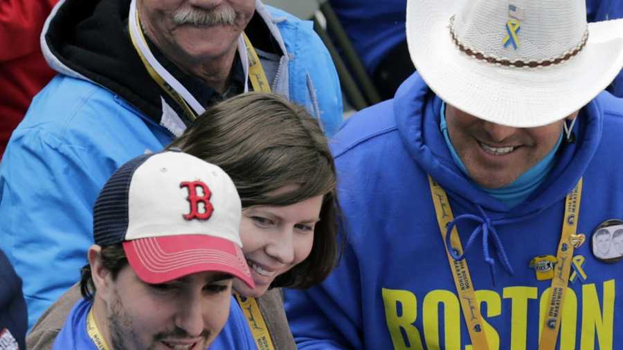 Boston Marathon bombing survivor Jeff Bauman waves an American flag alongside his fiancee Erin Hurley and Carlos Arredondo, right, the cowboy hat-wearing spectator who was hailed as a hero for helping the wounded after the bombings, near the finish line of the 118th Boston Marathon Monday, April 21, 2014 in Boston. 