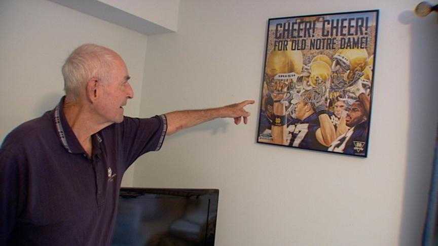 Ray Burtka points to a Notre Dame poster at his home. He has followed the Fighting Irish for most of his life.