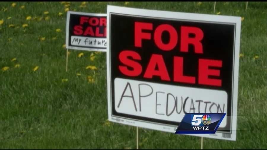Burlington High School students scatter "for sale" signs on school lawn representing dissatisfaction with budget cuts.