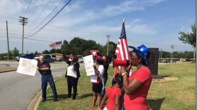 A group gathers along a busy Greenville intersection to ask drivers to honk against racism.