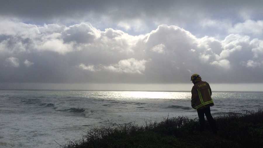 A firefighter searches for two people who were swept out to sea by big waves at Bonny Doon Beach.  (Jan. 19, 2016)