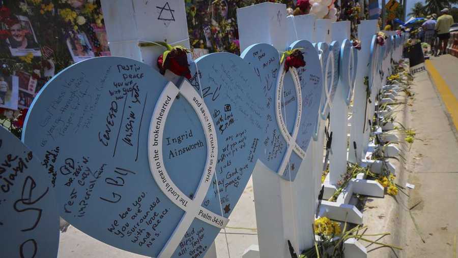 Wooden hearts with the names of victims are erected along side the photos, flowers, and other memorial items as visitors walk through the memorial site. 90 people have been confirmed dead due to the partial collapse of the Champlain Towers South in Surfside, Fla., on Sunday, July 11, 2021. (Carl Juste/Miami Herald via AP)