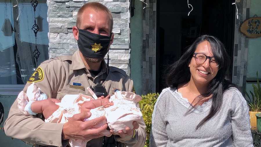 santa cruz county sheriff's deputy holds a baby that he saved from choking while standing next to the kid's mother.