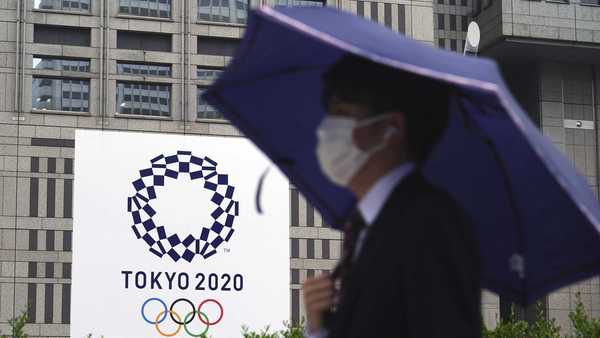 A man wearing a protective mask to help curb the spread of the coronavirus walks in the rain past a banner of Tokyo 2020 Olympic Games Thursday, May 13, 2021, in Tokyo.