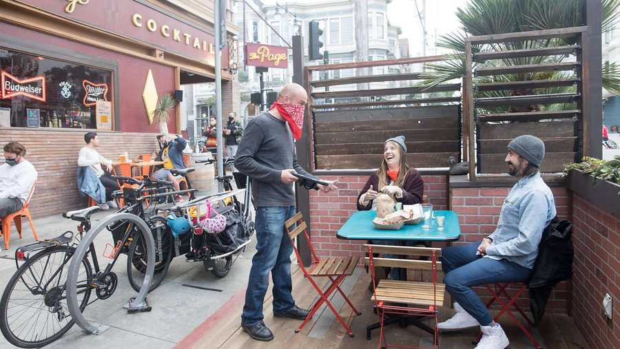 (Left to right) Waiter Riley Carter rings up the order of Jana Griffin and Corey Grosklos at The Page. Patrons dine and have drinks outside the bar on the sidewalk and parklet seating in San Francisco, Calif. on October 8, 2020.