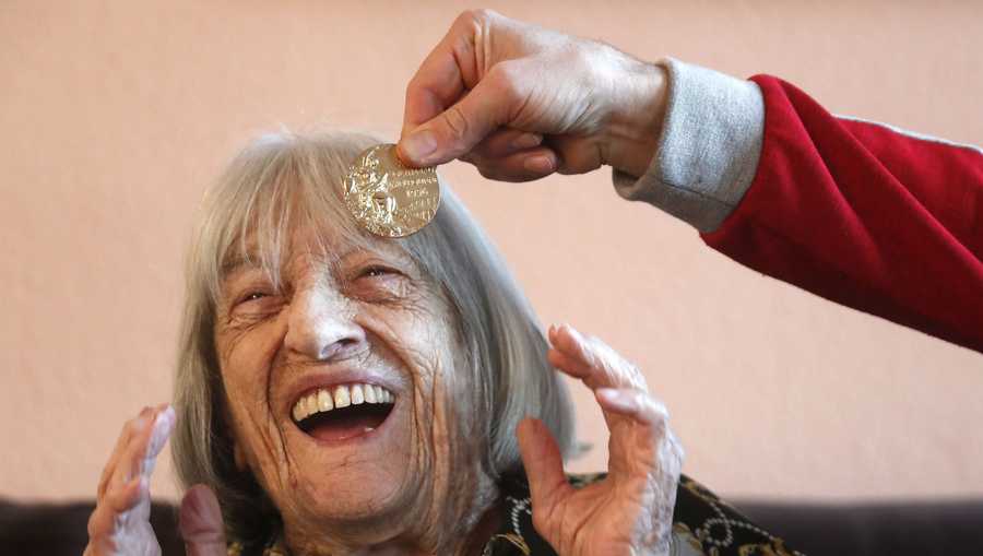 Agnes Keleti, former Olympic gold medal winning gymnast, laughs as her son Rafael holds one of her medals in front of her at her apartment in Budapest, Hungary Wednesday Jan. 8, 2020. Although she turned 99 on Thursday, even a 9-year-old would have a hard time keeping up with Agnes Keleti's irrepressible energy and enthusiasm. Keleti is the oldest living Olympic champion and a Holocaust survivor. She won 10 medals in gymnastics — including five golds — at the 1952 Helsinki Games and at the 1956 Melbourne Games.