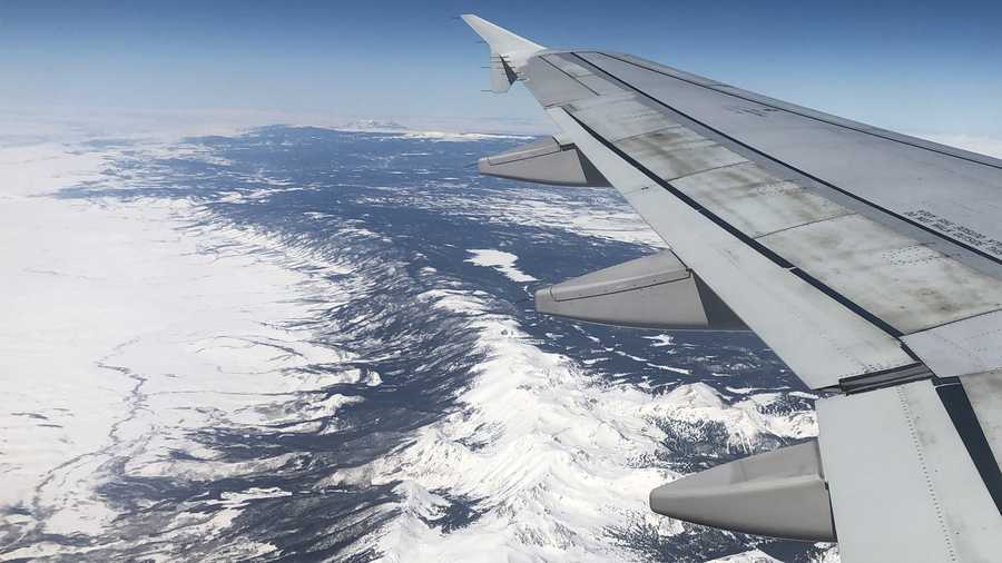A JetBlue plane flies across the snow-covered Colorado Rockies