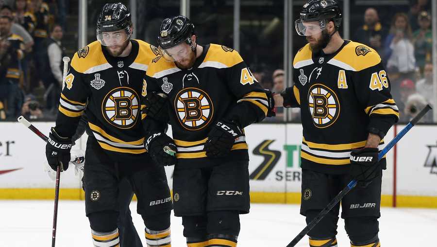 Boston Bruins' Matt Grzelcyk, center, is assisted from the ice by Jake DeBrusk, left, and David Krejci, right, after an injury during the first period in Game 2 of the NHL hockey Stanley Cup Final against the St. Louis Blues, Wednesday, May 29, 2019, in Boston. (AP Photo/Michael Dwyer)