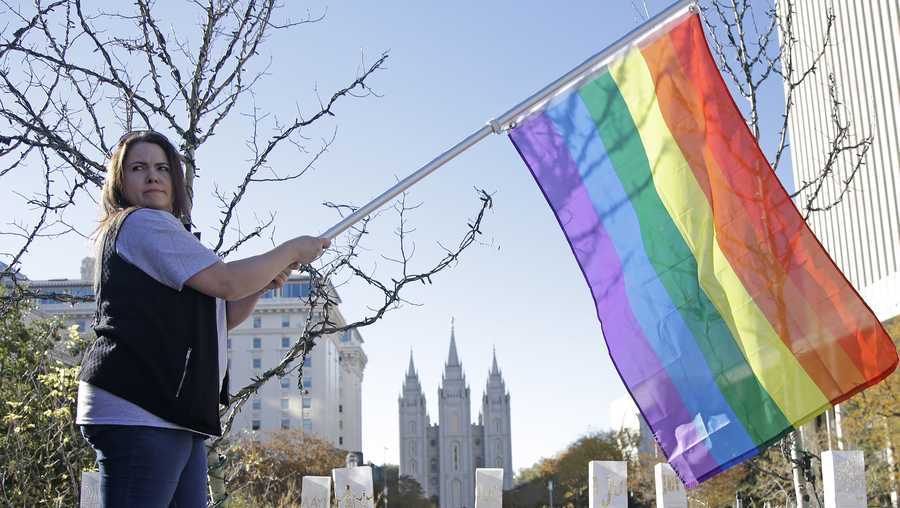 FILE - In this Nov. 14, 2015, file photo, Sandy Newcomb poses for a photograph with a rainbow flag as Mormons gather for a mass resignation from the Church of Jesus Christ of Latter-day Saints in Salt Lake City. The Mormon church's massive genealogical database will begin accepting submissions of names of people from same-sex relationships sometime next year. The move doesn't foreshadow any change to long-standing church opposition to gay marriage, but it is being done to ensure the databank has as much information as possible for researchers, according to a statement from The Church of Jesus Christ of Latter-day Saints.