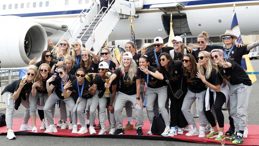 Members of the United States women's soccer team, winners of a fourth Women's World Cup, pose with the trophy by their plane after arriving at Newark Liberty International Airport, Monday, July 8, 2019, in Newark, N.J. Julie Ertz holds the trophy, Megan Rapinoe, front right, gestures, and Alex Morgan, back left, also gestures. (AP Photo/Kathy Willens)