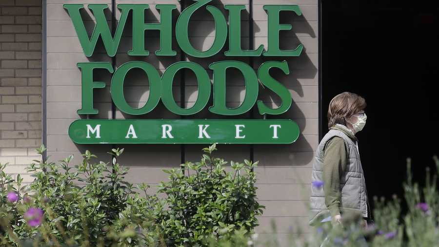 A pedestrian wears a mask while walking past a sign for a Whole Foods Market in San Francisco, Tuesday, March 31, 2020. (AP Photo/Jeff Chiu)
