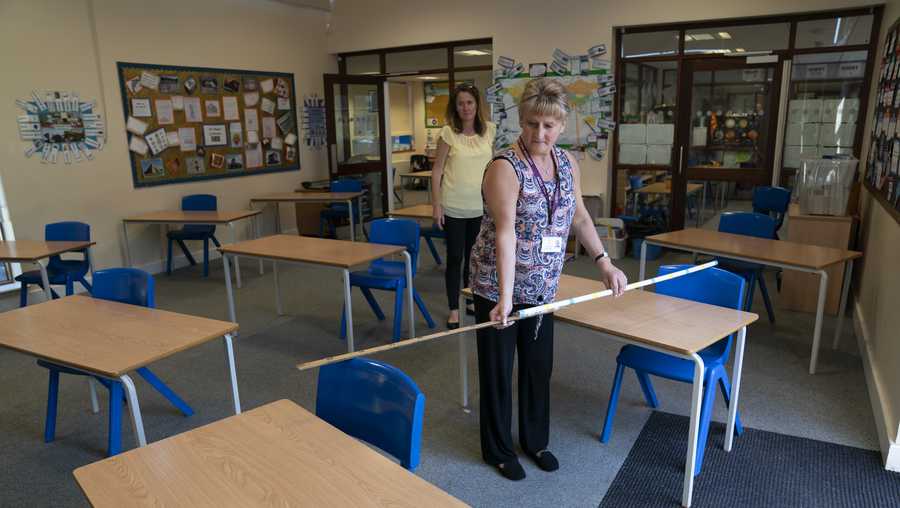 Year 6 teacher Jane Cooper uses a 2 meter length of ruler and pipe to check seat spacings in her classroom as measures are taken to prevent the transmission of coronavirus before the possible reopening of Lostock Hall Primary school in Poynton near Manchester, England, Wednesday May 20, 2020. (AP Photo/Jon Super)