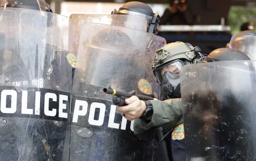 A policeman shoots rubber bullets at protesters throwing rocks and water bottles during a demonstration next to the city of Miami Police Department, Saturday in downtown Miami.