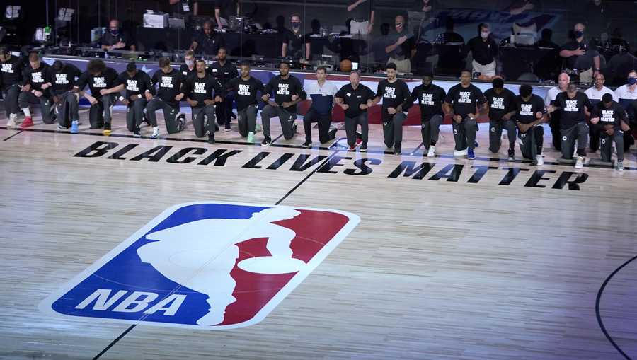 Members of the Milwaukee Bucks and the Boston Celtics kneel around a Black Lives Matter logo before the start of an NBA basketball game Friday, July 31, 2020, in Lake Buena Vista, Fla. (AP Photo/Ashley Landis, Pool)