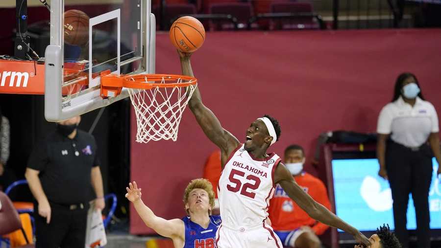 Oklahoma forward Kur Kuath (52) goes up for a dunk in front of Houston Baptist guard Brycen Long (3) and guard Pedro Castro, right, in the first half of an NCAA college basketball game Saturday, Dec. 19, 2020, in Norman, Okla. (AP Photo/Sue Ogrocki)