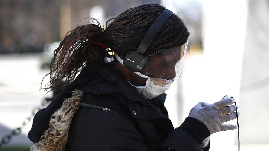 A woman wears protective gloves, mask and face shield while waiting for a bus in Detroit, Wednesday, April 8, 2020.