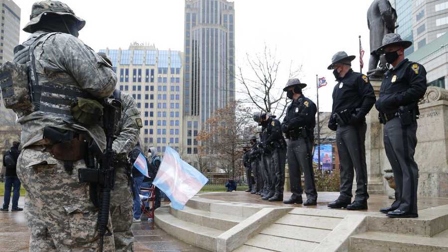 Ohio state troopers provide security at the Ohio Statehouse as armed protestors look on Sunday, Jan. 17, 2021, in Columbus, Ohio. Security was stepped up at statehouses across the U.S. after FBI warnings of potential armed protests at all 50 state capitols and in Washington, D.C. (AP Photo/Jay LaPrete)