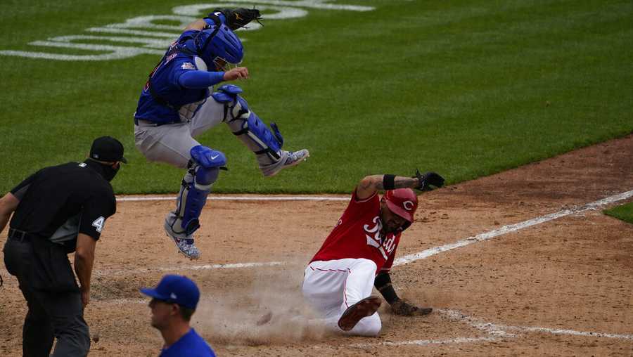 Chicago Cubs catcher Tony Wolters (11) leaps as Cincinnati Reds&apos; Nick Castellanos (2) scores on an RBI single hit by Cincinnati Reds&apos; Eugenio Suarez (7) in the sixth inning during a baseball game against the Chicago Cubs in Cincinnati on Sunday, May 2, 2021. (AP Photo/Jeff Dean)wld