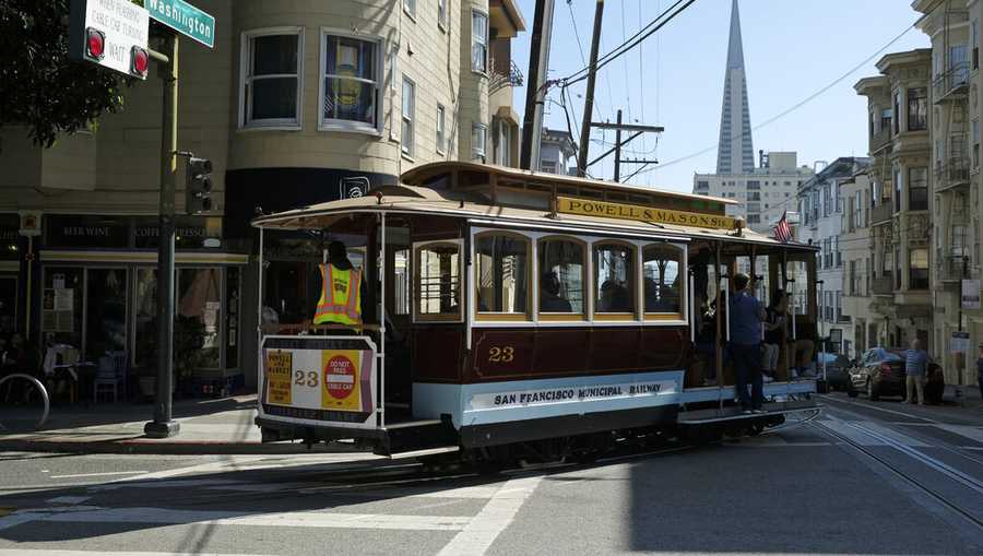 FILE - In this Sept. 11, 2019, file photo, a cable car turns onto Washington Street with the Transamerica Pyramid in the background in San Francisco. San Francisco&apos;s iconic cable cars remain sidelined by the coronavirus pandemic but officials said Friday, May 14, 2021, the city&apos;s historic streetcars will start rolling again this weekend.(AP Photo/Eric Risberg, File)
