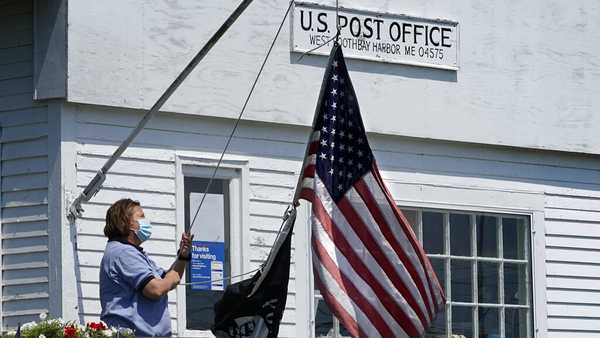 An employee raises the American flag outside a branch of the U.S. Post Office, Wednesday, July 7, 2021, in West Boothbay Harbor, Maine. Many post offices still require the use of face coverings due to COVID-19. (AP Photo/Robert F. Bukaty)