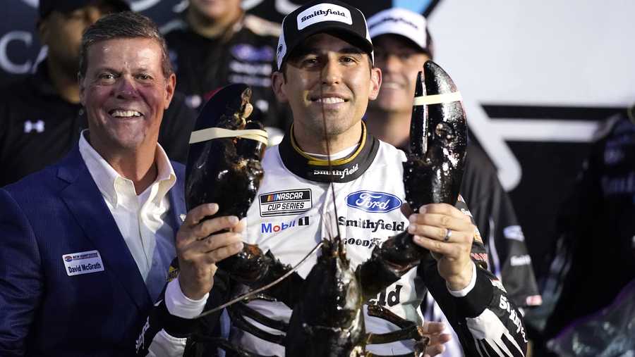 Aric Almirola smiles as he holds up a giant lobster after winning the NASCAR Cup Series auto race Sunday, July 18, 2021, in Loudon, N.H. At left is Dave McGrath, general manager of New Hampshire Motor Speedway. (AP Photo/Charles Krupa)