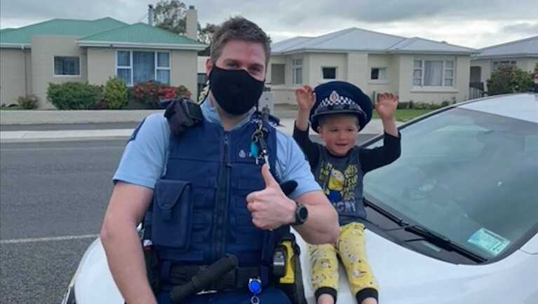 In this photo released by New Zealand Police, an officer identified only as Constable Kurt sits on his patrol car with a 4-year-old boy who is not identified, in the South Island city of Invercargill, New Zealand, Friday, Oct. 15, 2021.  (NZ Police via AP)