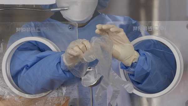 A medical worker wearing protective gear in a booth, wears plastic gloves at a temporary screening clinic for the coronavirus in Seoul, South Korea, Monday, Nov. 29, 2021. (AP Photo/Lee Jin-man)
